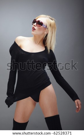 Blond lady in black stylish lingerie and fashionable sunglasses posing in the studio on a dark gray background