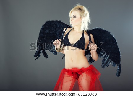 Pretty blond woman in black lingerie with angel wings on a dark gray background