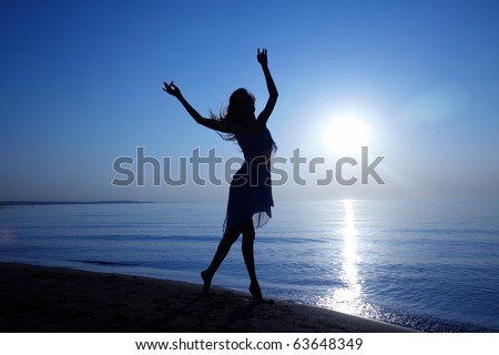 Silhouette of the woman with long hairs dancing at the beach during sunset. Artistic colors added
