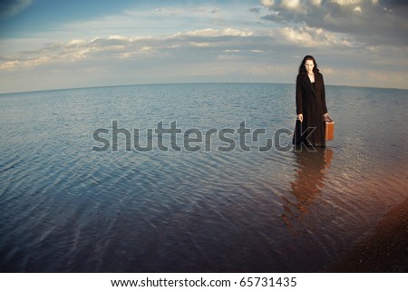 Alone woman in the coat holding case and standing in the sea