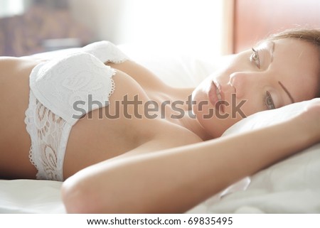 Pensive sensual woman laying in the bedroom at the early morning. Natural colors and sunlight from the window