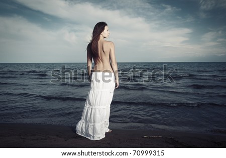 Single lady with naked back standing at the cold sea. Artistic colors added