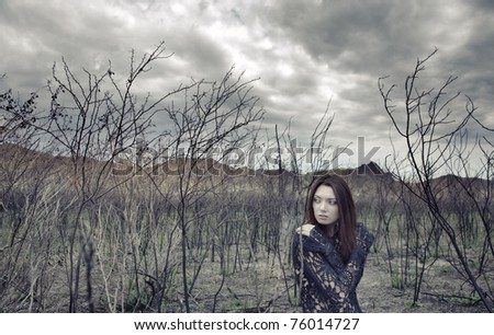 Sad alone woman in the dead bushes and thunderous sky on a background. Artistic colors added for movie effect
