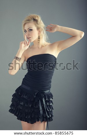 Blond lady in black dress making finger on lips in the studio
