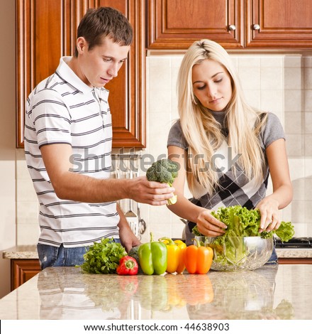Young couple in kitchen make salad with fresh vegetables. Square shot.