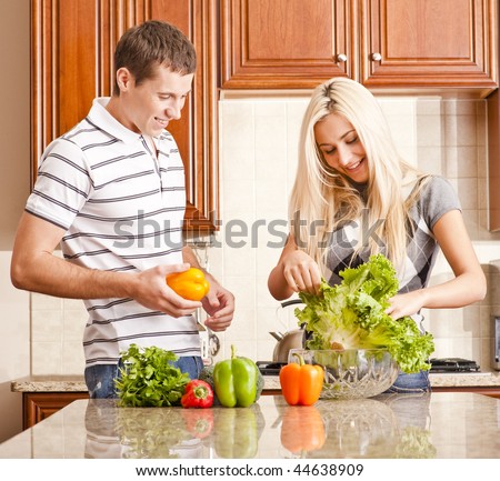 Young couple in the kitchen enjoy preparing salad with fresh vegetables. Square shot.