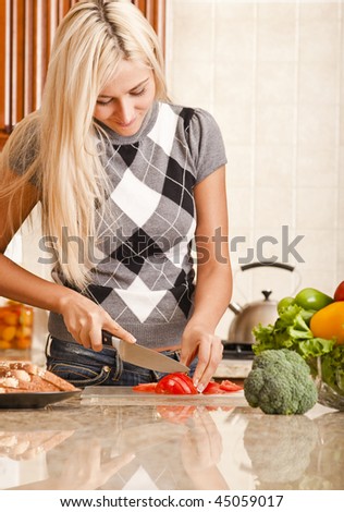 Young woman cutting up tomato in kitchen for meal. Vertical shot.