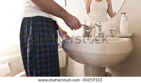Man holding razor in white porcelain sink with water running from the faucet. Horizontal shot.