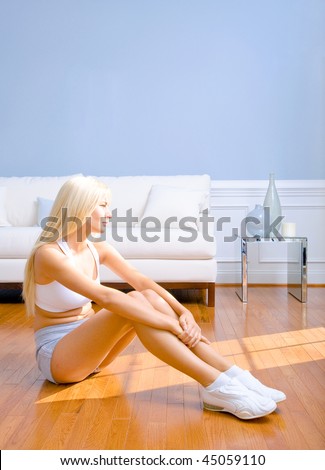 Young woman sitting on floor with arms around drawn up knees. Vertical shot.