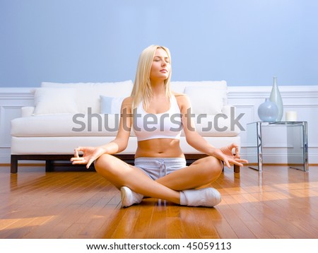 Young woman sitting cross legged on floor with hands on knees meditating. Horizontal shot.