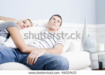 Woman snuggles up to man as they both relax quietly on a white couch. Horizontal format.