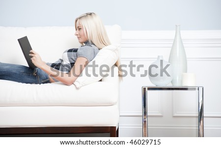 Cropped view of a woman relaxing on a white couch and reading a book. Horizontal format.