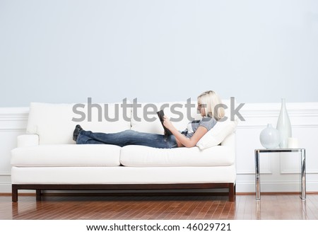 Full length view of woman reclining on white couch and reading a book. Horizontal format.