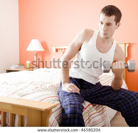Cropped view of man sitting on bed with a blank expression and using an arm weight. Square format.
