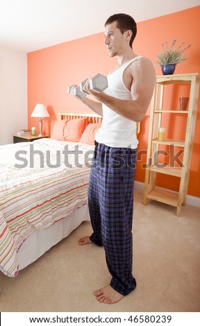 Full length view of man standing next to bed and lifting arm weights. Vertical format.