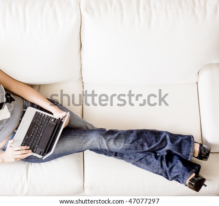 Cropped overhead view of woman reclining on white couch and using a laptop. Horizontal format.