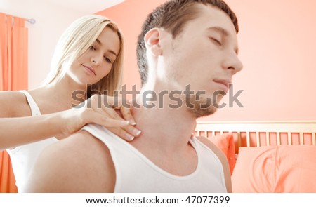 Man and woman sit on bed as woman massages man\'s shoulders. Horizontal format.