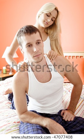 Man and woman sit on bed as woman massages man\'s shoulders. Vertical format.