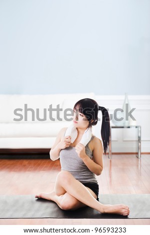 Portrait of a sitting Asian woman holding a towel around her neck after a workout.