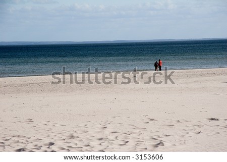 two lonely people walking on the sandy beach