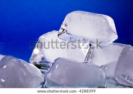 Melting ice cubes with water drops on a mirror - blue background