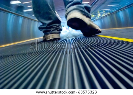 Man\'s foot walking in airport escalator perspective view (ground level)