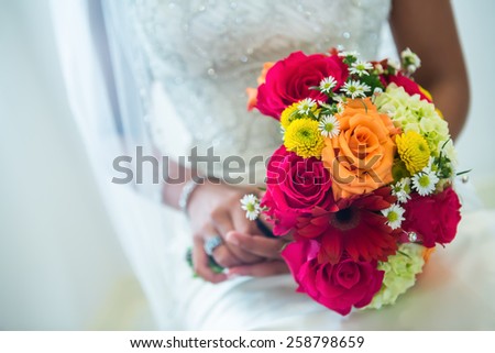 Beautiful orange, red, and yellow bouquet loaded with daisies and roses in the hands of a beautiful ethnic bride.