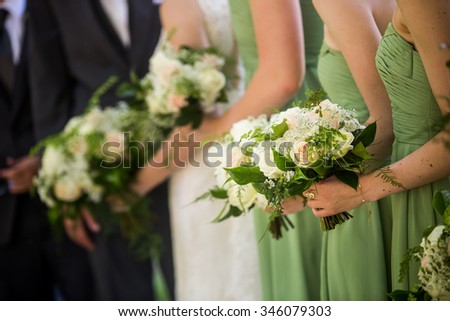 A candid photo of bride and her bridesmaids wearing light green bridesmaid dresses and holding a gorgeous bouquet. White and pink roses with baby\'s breath and green accents.