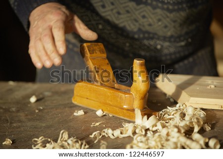Old cabinet-maker is working with wood planer in his workshop.