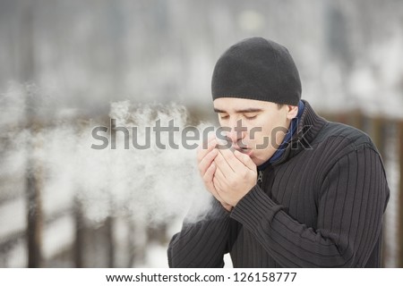 Young man in winter landscape and warmed the hands of breath