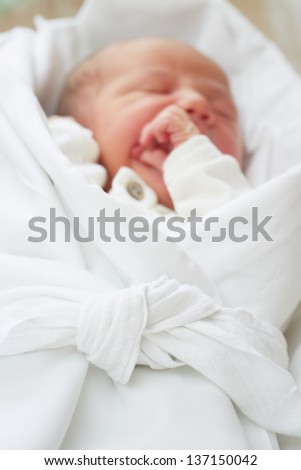 Newborn baby is peacefully sleeping in wrap - selective focus on knot