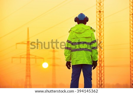 Worker is watching electricity pylons and substation at the sunrise