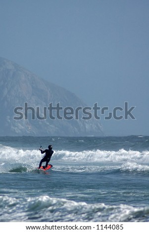 Kite surfer ( kite boarder ) riding the waves with Morro Rock in the background near Cayucos, California.
