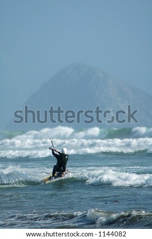 Kite surfer ( kite boarder ) riding the waves with Morro Rock in the background near Cayucos, California.