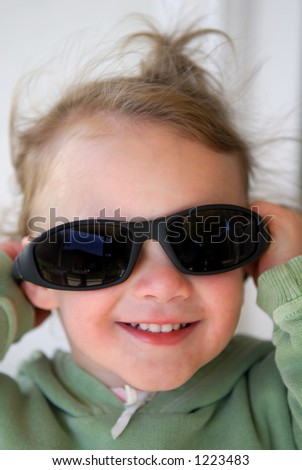 An adorable laughing 2 year old laughs as she playfully tries on a pair of sunglasses.