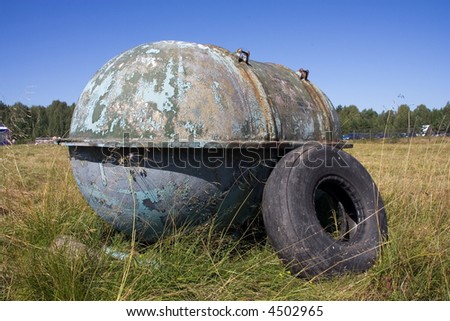 a photo of an old and neglected fuel tank and a plane tire lying on a field