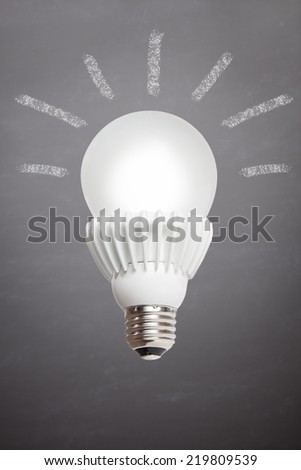 A lit LED bulb is set against a slate background with idea rays coming form the bulb