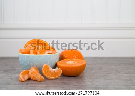 Mandarin orange slices in a blue bowl on a wooden table with unsliced orange nearby
