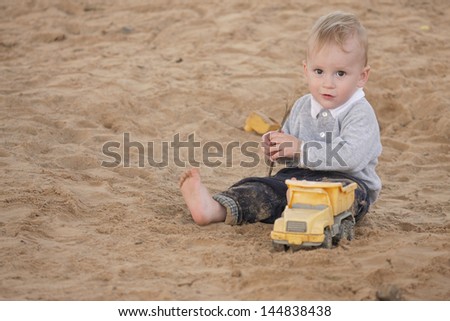 Boy sitting in sandpit and playing with toys