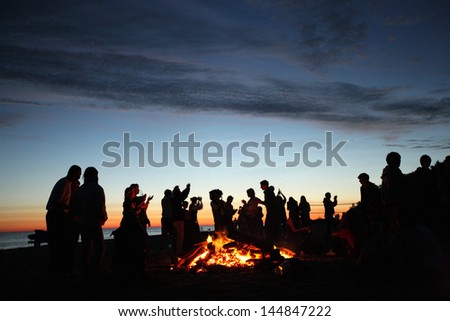 People celebrating in evening at the beach next to fire