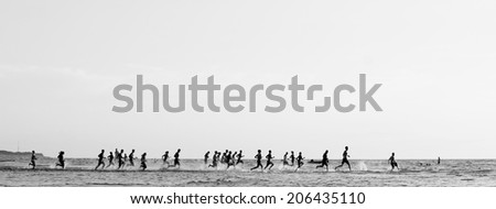 Monochrome sea landscape; crowd of people racing one another running into the sea
