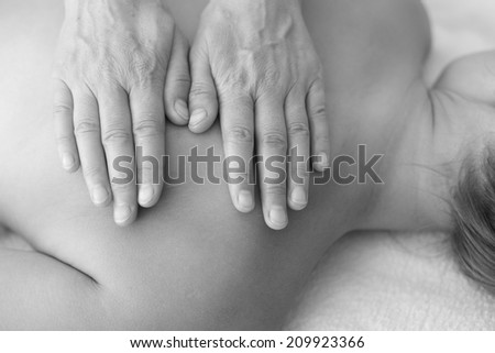 Hands of massage therapist on woman\'s back; monochrome