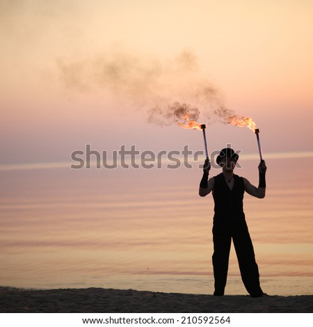 Stylish man with pair of burning juggling torches on the beach