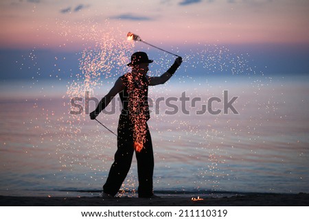 Fire dancer silhouette on sunset sky background