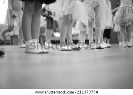 Legs of small girls in gymnastic slippers and fluffy skirts; monochrome