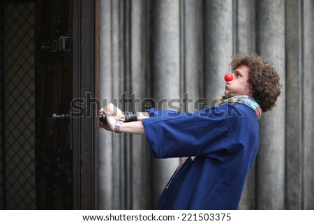 Profile of funny clown opening heavy doors; street theater concept