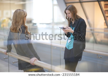 Young women standing in the office corridor, a woman using smart-phone seeking for information