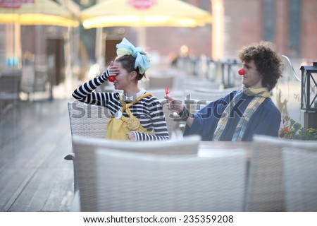 Clowns dating, man gives a flower, shy woman covering eyes; street theater concept