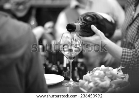 Hands of bartender pouring wine into a glass goblet, monochrome