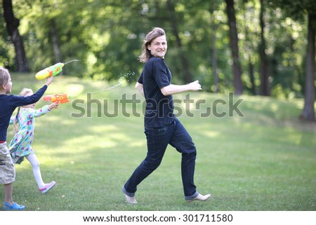 Young father running away from children with water blasters